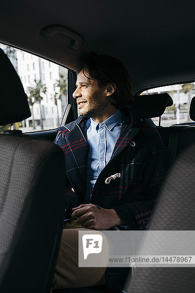 Lächelnder Mann sitzt auf dem Rücksitz eines Autos und schaut aus dem Fenster