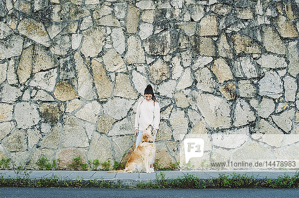 Junge Frau mit ihrem Golden-Retriever-Hund an einer Steinmauer