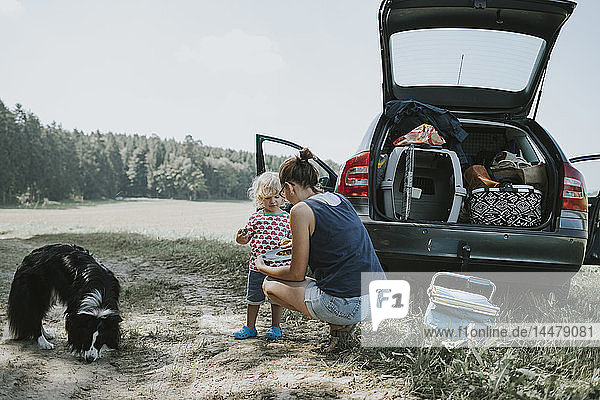 Mother and toddler with dog at a car on the countryside