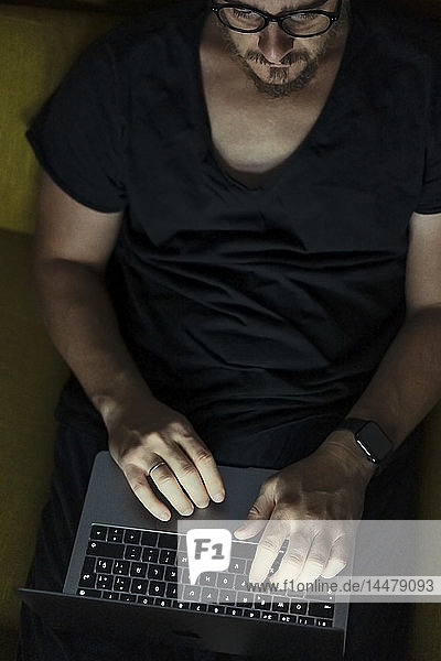 Man sitting on couch using laptop at night