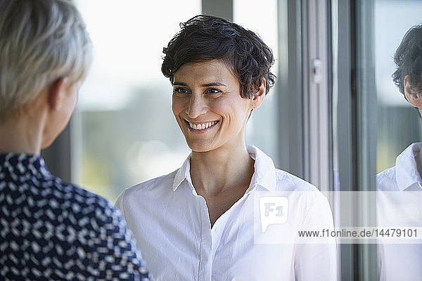Portrait of smiling smiling businesswoman looking at colleague at the window in office