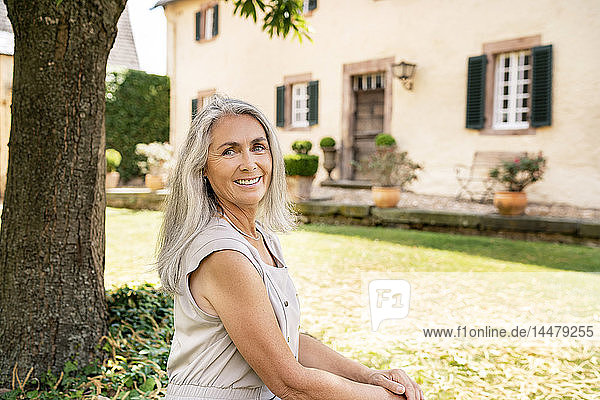 Bildnis einer lächelnden Frau mit langen grauen Haaren im Garten