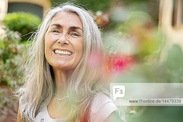 Bildnis einer glücklichen Frau mit langen grauen Haaren im Garten