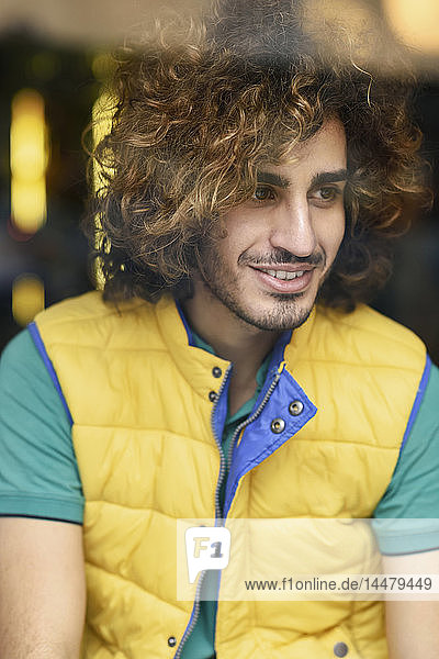 Portrait of smiling young man with beard and curly hair wearing yellow waistcoat looking out of window