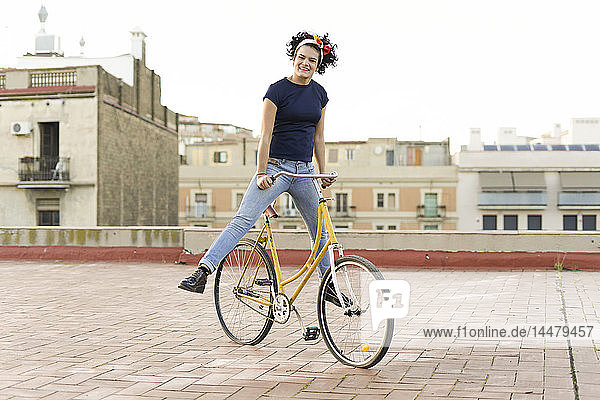 Porträt einer glücklichen jungen Frau  die auf dem Fahrrad in der Stadt balanciert