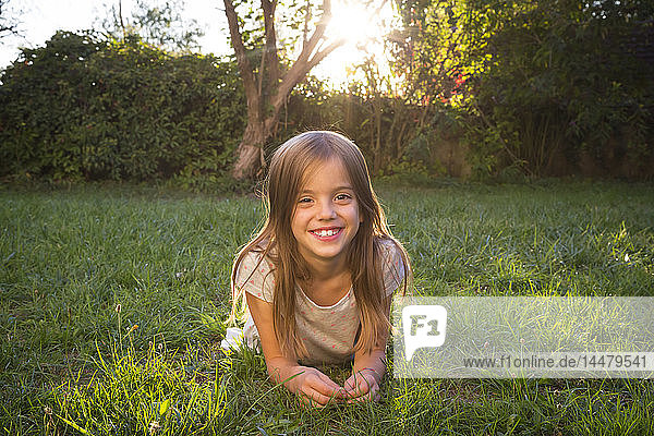 Porträt eines lächelnden kleinen Mädchens  das in der Abenddämmerung auf einer Wiese liegt