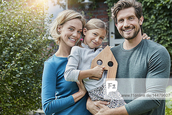 Porträt einer glücklichen Familie vor ihrem Haus mit Hausmodell