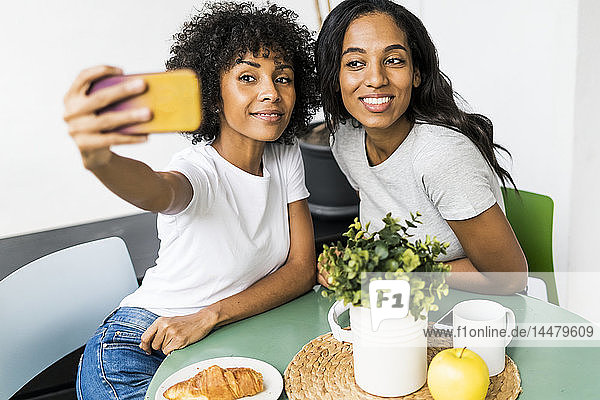 Zwei glückliche Freundinnen sitzen am Tisch und machen ein Selfie