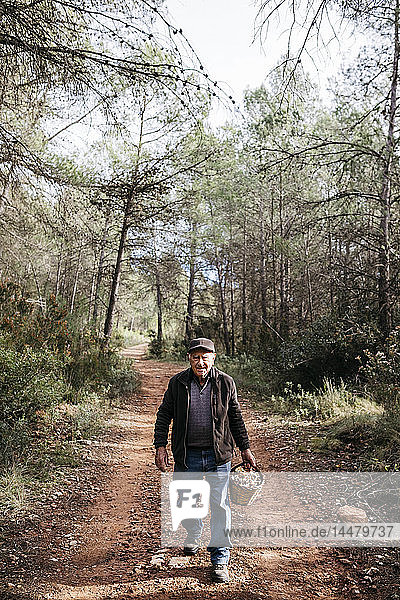 Portrait of smiling senior man walking with basket full of mushrooms in the forest