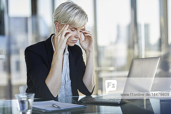 Erschöpfte Geschäftsfrau sitzt mit geschlossenen Augen am Schreibtisch im Büro