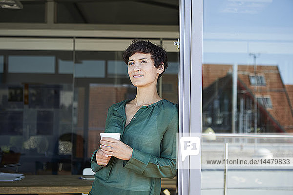 Lächelnde Frau steht am Fenster und macht eine Kaffeepause
