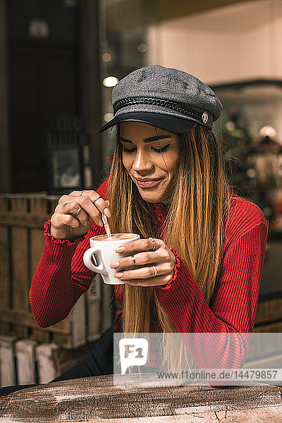 Porträt einer lächelnden jungen Frau  die auf der Terrasse eines Cafés sitzt und Kaffee rührt