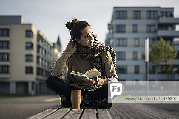 Melancholische Frau mit Kaffee zum Buchen im Herbst auf der Bank sitzend