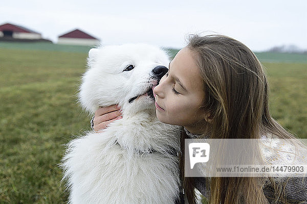 Mädchen und ihr weißer Hund kuscheln auf einer Wiese