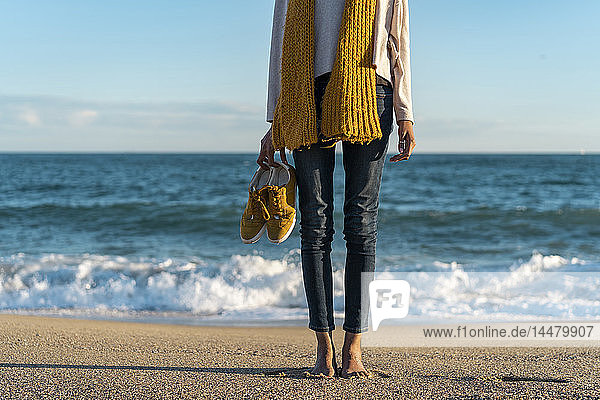 Barfüßige Frau am Strand  die ihre Schuhe trägt