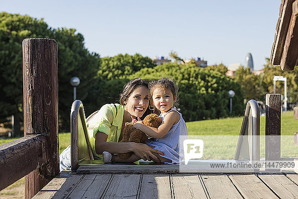 Lächelnde Mutter mit Tochter auf einer Rutsche auf einem Spielplatz