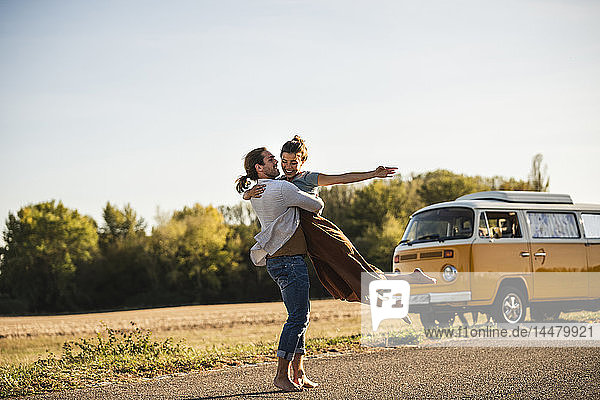 Glückliches Paar  das mit einem Wohnmobil unterwegs ist und sich auf der Straße umarmt