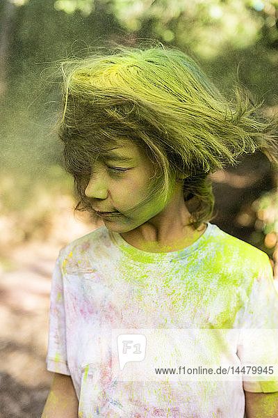 Junge schüttelt den Kopf  voller bunter Pulverfarbe  feiert Holi  das Fest der Farben