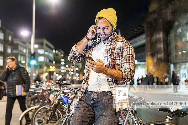 Großbritannien  London  Mann  der nachts in der Stadt pendelt und auf sein Telefon schaut