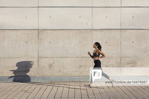 Young woman running along concrete wall in the city