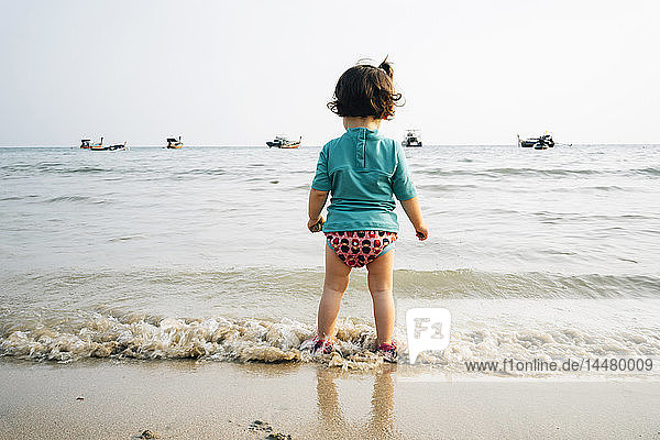 Thailand  Koh Lanta  back view of baby girl wearing UV protection shirt standing at seashore