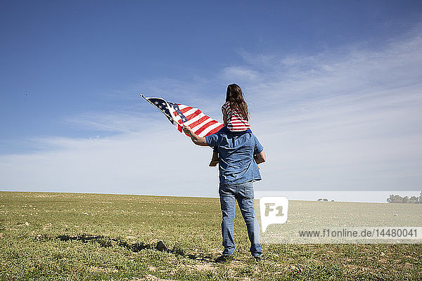 Man with daughter and American flag standing on field in remote landscape