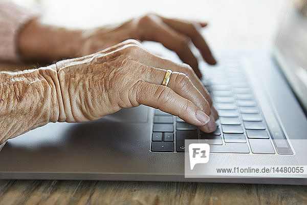 Hand of senior woman typing on keyboard of laptop  close-up