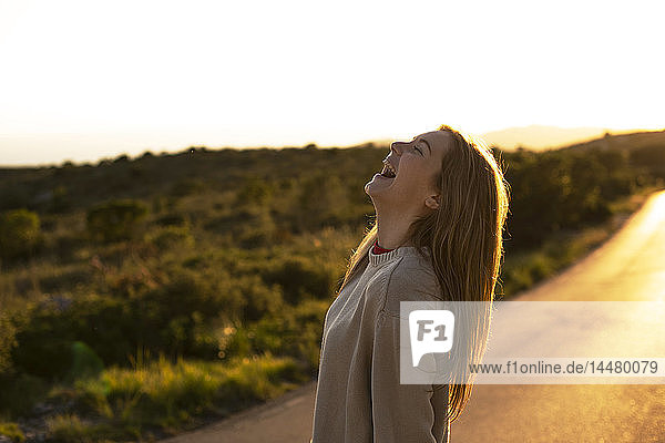 Laughing young woman on country road at sunset