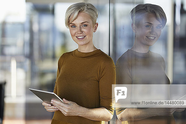 Porträt einer lächelnden Geschäftsfrau mit Tablette am Fenster
