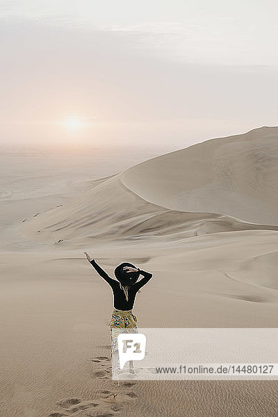 Namibia  Namib  Rückenansicht einer modischen Frau  die auf einer Wüstendüne springt