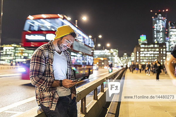 UK  London  smiling man using phone at the street in the city at night