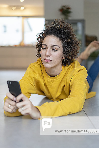 Frau liegt zu Hause auf dem Boden und benutzt ihr Handy