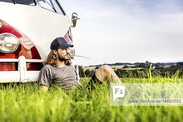 Junger Mann sitzt in einem Lieferwagen auf einem Feld in ländlicher Landschaft