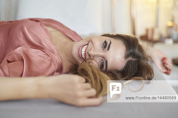 Porträt einer glücklichen jungen Frau im Bademantel im Bett liegend