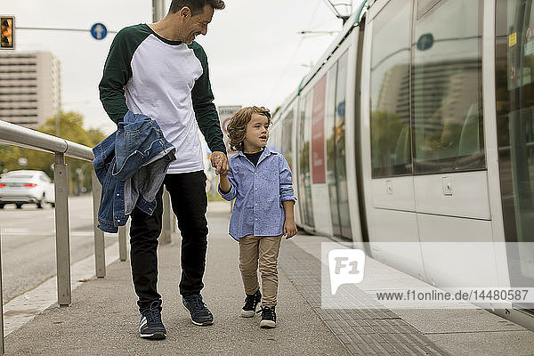 Smiling father and son walking hand in hand at tram stop in the city