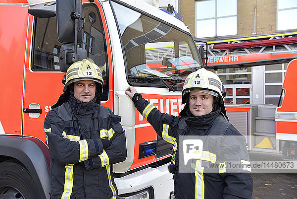 Portrait of two confident firefighters in front of fire engine