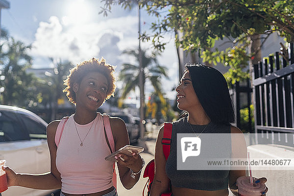 USA  Florida  Miami Beach  two happy female friends with cell phone and soft drink in the city