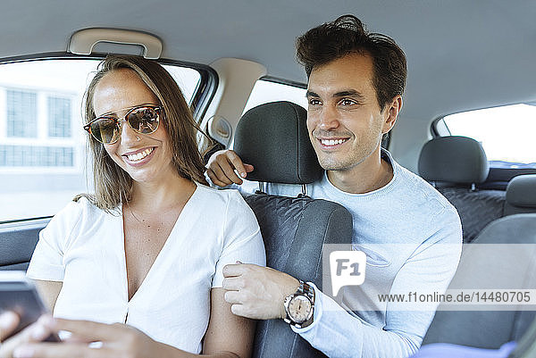 Glückliches Paar im Auto mit Mann auf dem Rücksitz und Frau mit Handy auf dem Beifahrersitz