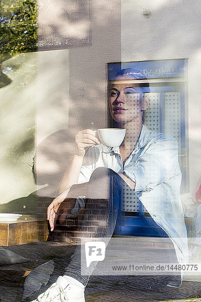 Frau sitzt in einem Café und trinkt eine Tasse Kaffee  während sie aus dem Fenster schaut