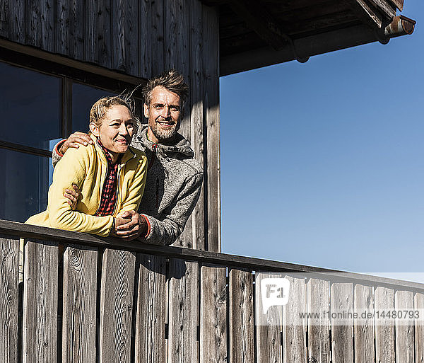 Couple leaning on balcony of a mountain hut  with arms around