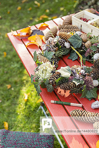 Herbstlicher Kranz mit Hortensien,  Tannenzapfen und Efeu auf Gartentisch
