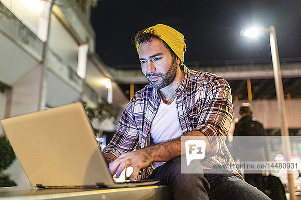 UK  London  smiling man using laptop out in the city at night