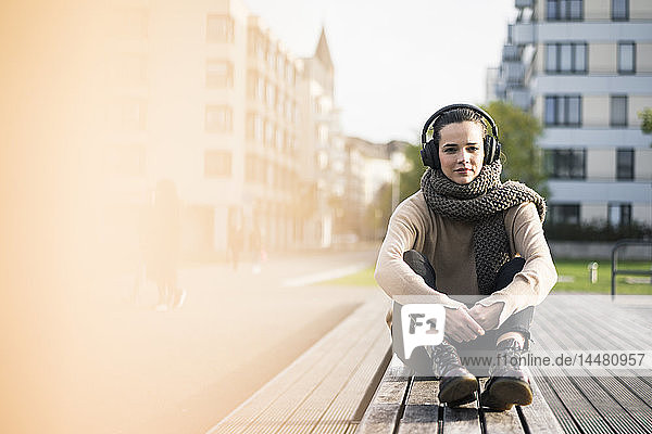 Porträt einer Frau  die im Herbst auf einer Bank sitzt und mit schnurlosen Kopfhörern Musik hört