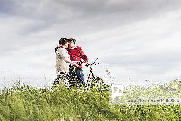 Älteres Ehepaar mit Fahrrädern küsst sich in ländlicher Landschaft