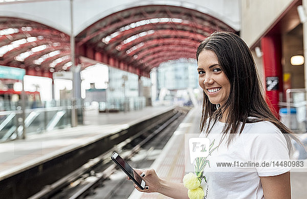 UK  London  portrait of smiling young woman holding cell phone in a train station