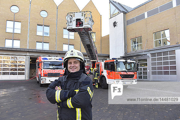 Portrait of smiling firefighter in front of fire engine with colleagues in background