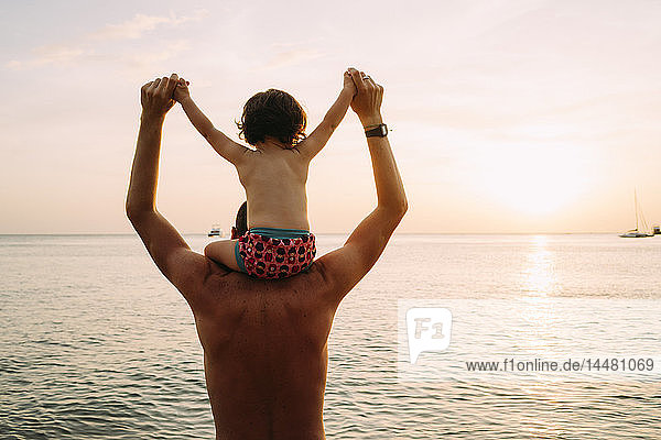 Thailand  Koh Lanta  Rückenansicht eines Vaters mit einem kleinen Mädchen auf den Schultern beim Sonnenuntergang am Strand