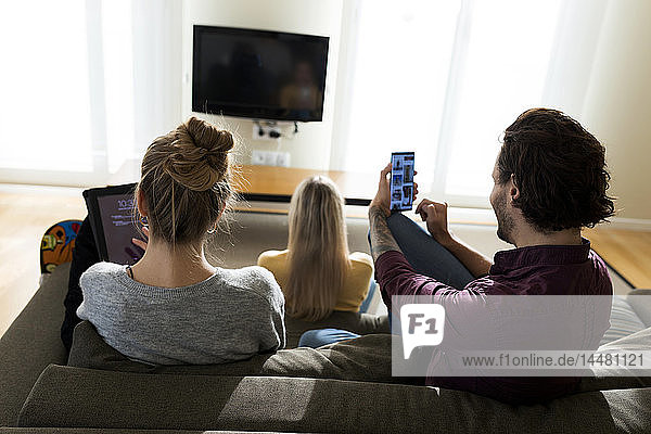 Freunde sitzen auf der Couch im Wohnzimmer und benutzen digitale Geräte