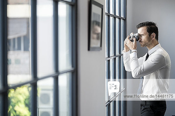 Businessman taking picture with vintage retro camera in front of large office window