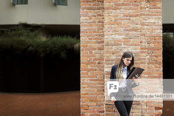 Junge Geschäftsfrau steht mit Tablette an Backsteinsäule
